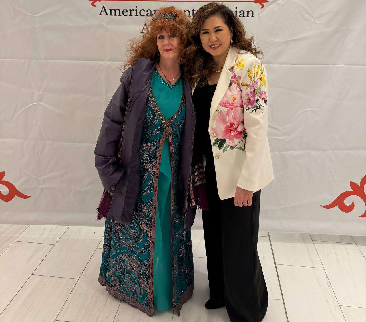 Two community members in traditional dress posing before an event backdrop