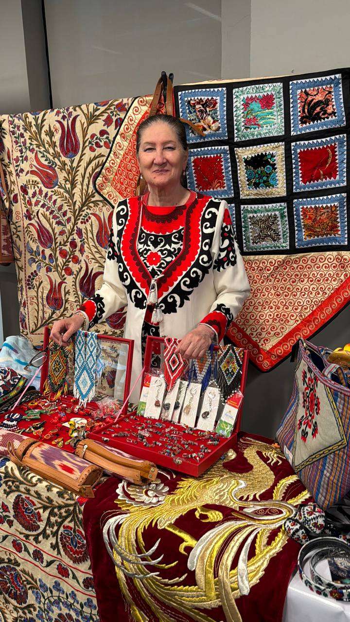 Woman in traditional dress presenting embroidered textiles and jewelry