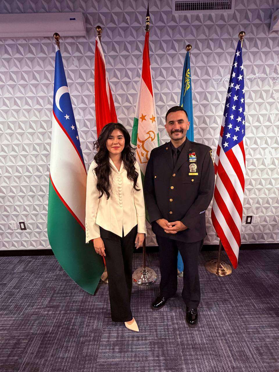 Community member and a police officer standing together before a row of flags