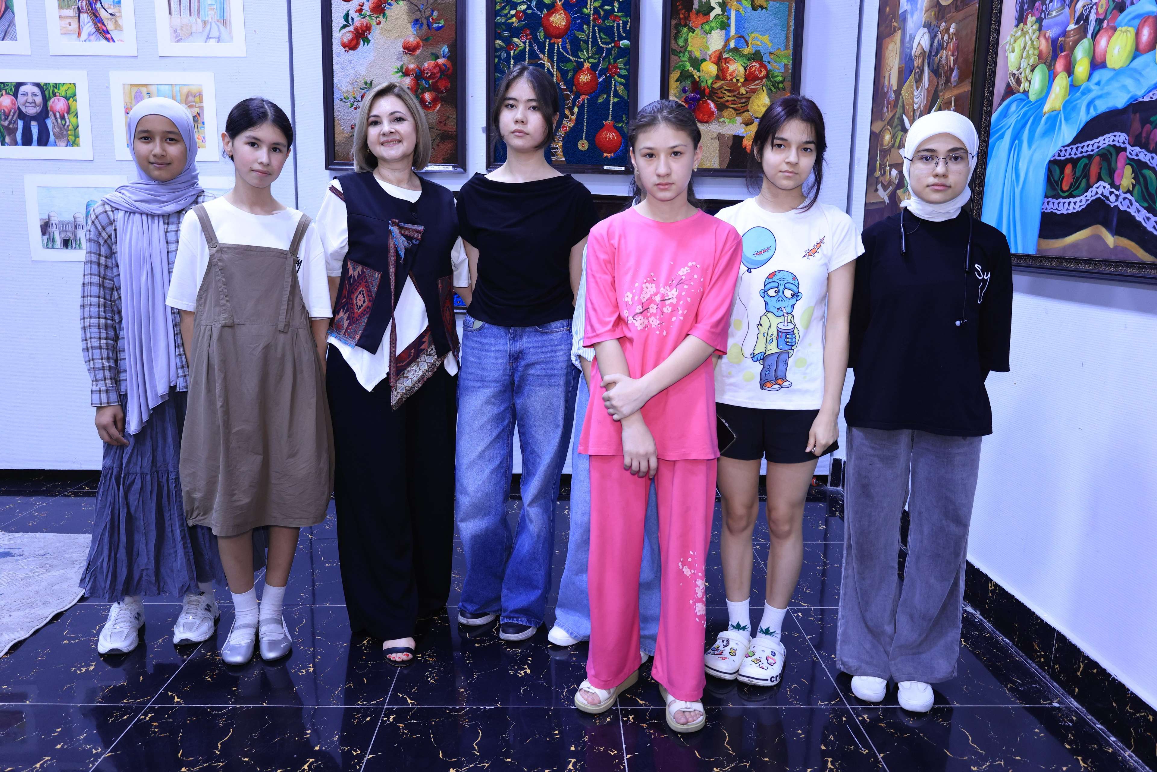 Young participants standing together at an art exhibition, artwork displayed on the wall behind them