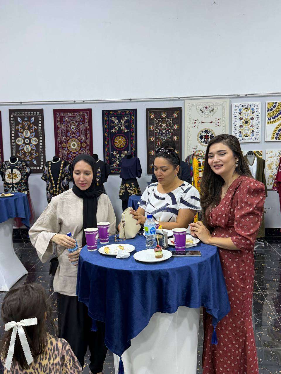Guests sharing tea at an exhibition opening, embroidered panels on the wall
