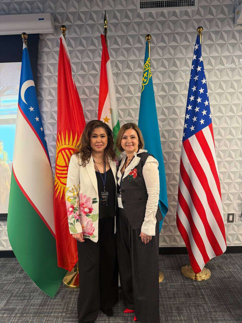 Two community members standing before the flags of the United States and Central Asian nations