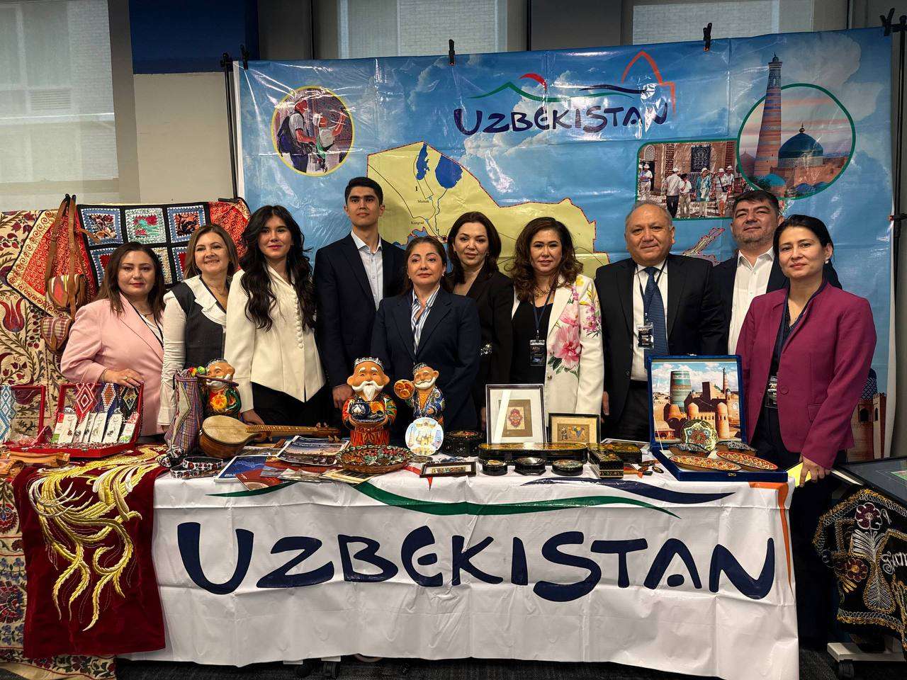 Community members at a cultural display table with crafts, books, and a banner reading Uzbekistan