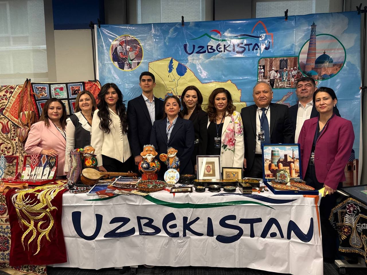 Community members at a cultural display table with crafts, books, and a banner reading Uzbekistan