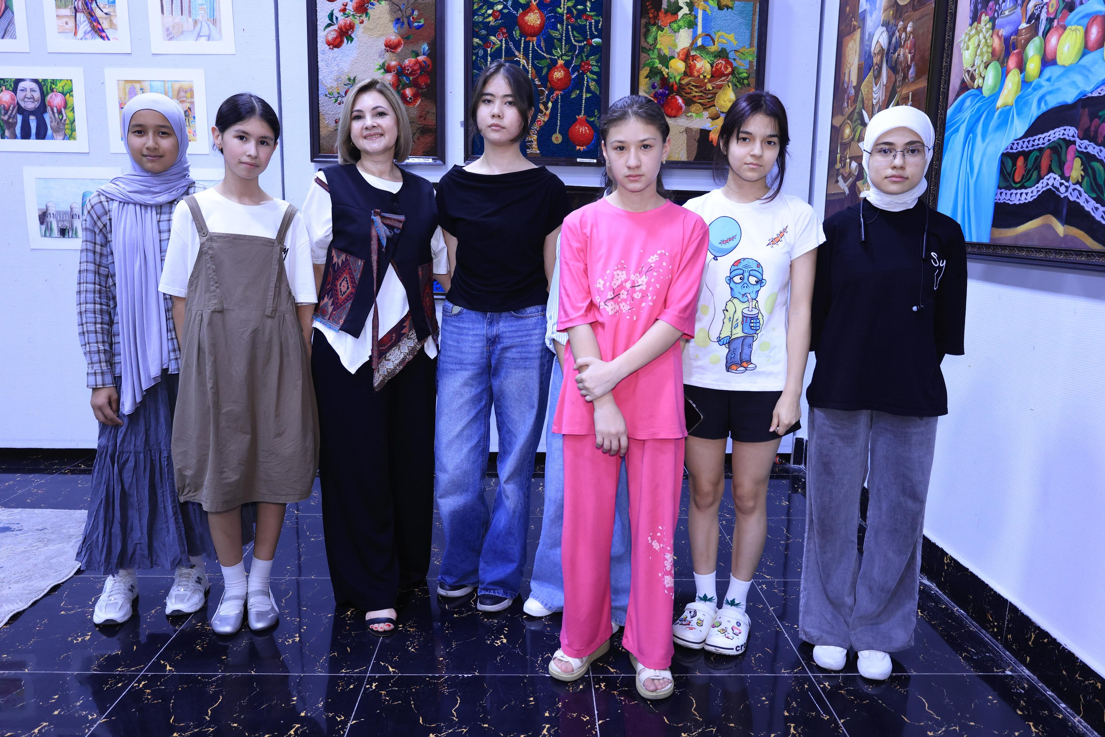 Young participants standing together at an art exhibition, artwork displayed on the wall behind them