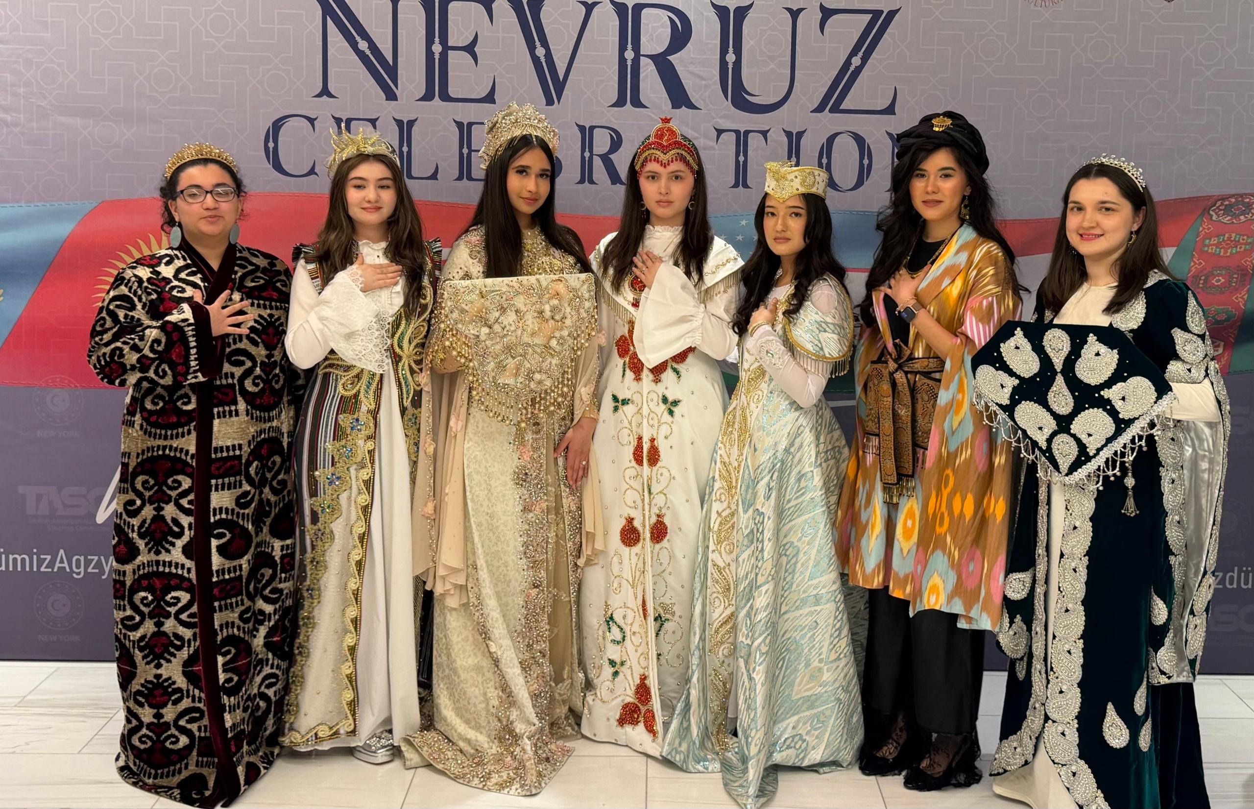 Young women in traditional gowns and crowns posing before a Nevruz Celebration backdrop